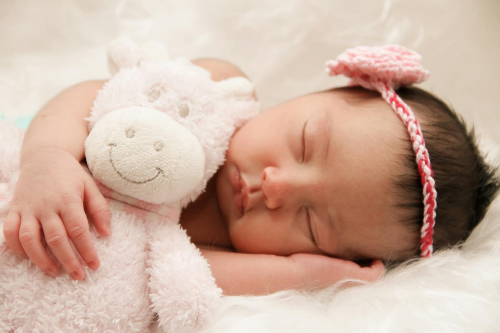 Adorable sleeping baby cuddling a plush toy, wearing a cute pink headband.